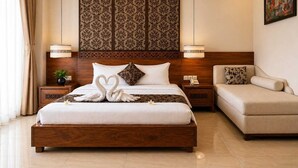 A hotel room with a large bed, a sofa, a nightstand with a lamp, and a decorative headboard.