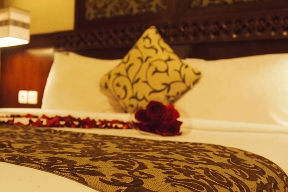 Una cama con ropa de cama estampada, un cojín decorativo y una rosa roja.