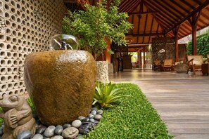 A stone fountain, a wooden deck, and a seating area with chairs. - Yulia Village Inn (Ubud)