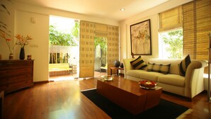 A modern living room with a sofa, coffee table, and a wooden cabinet. There is a large window with blinds and a painting on the wall. - juSTa OFF MG Road (Bengaluru)