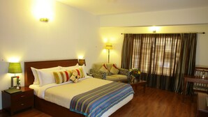 A hotel room with a large bed, a sofa, a desk, and a window with curtains. - juSTa OFF MG Road (Bengaluru)