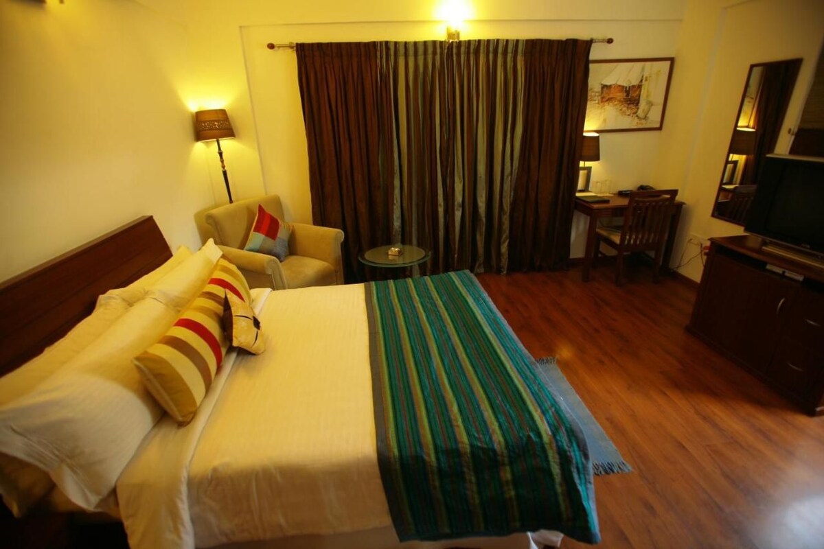 A hotel room with a bed, a chair, a desk, a television, and curtains.