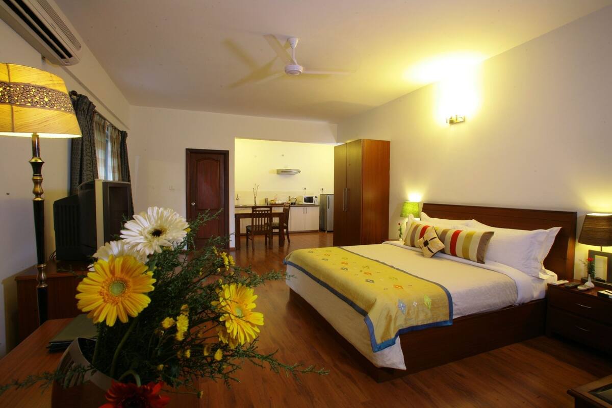 A hotel room with a bed, bedside table, lamp, and a bouquet of flowers.