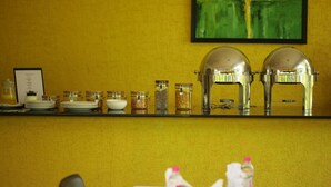A hotel reception area with a yellow wall, a framed abstract painting, a counter with glass jars of condiments, and a water dispenser. - juSTa OFF MG Road (Bengaluru)