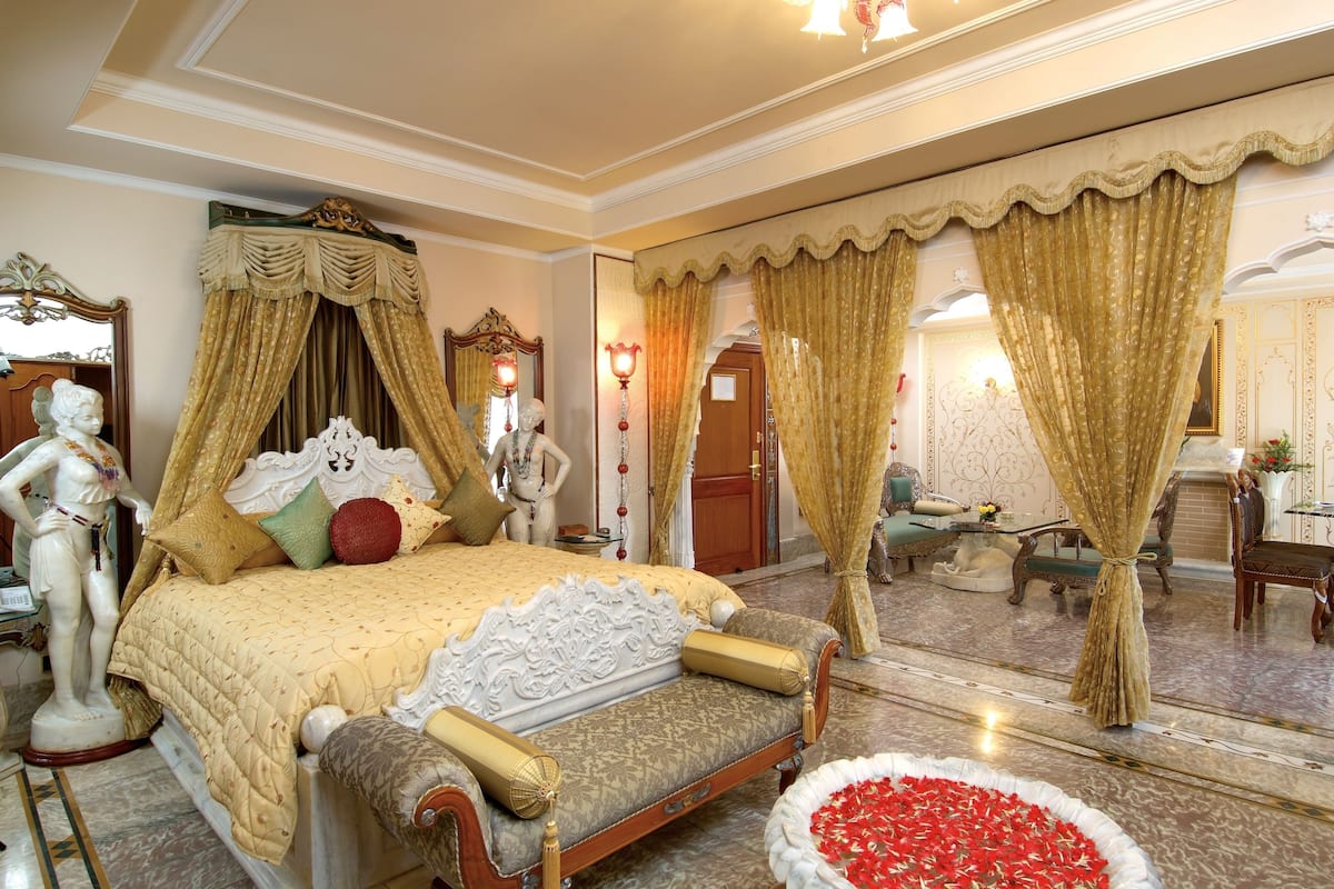 Un dormitorio lujoso con cama con dosel, cortinas ornamentales y un espejo decorativo.