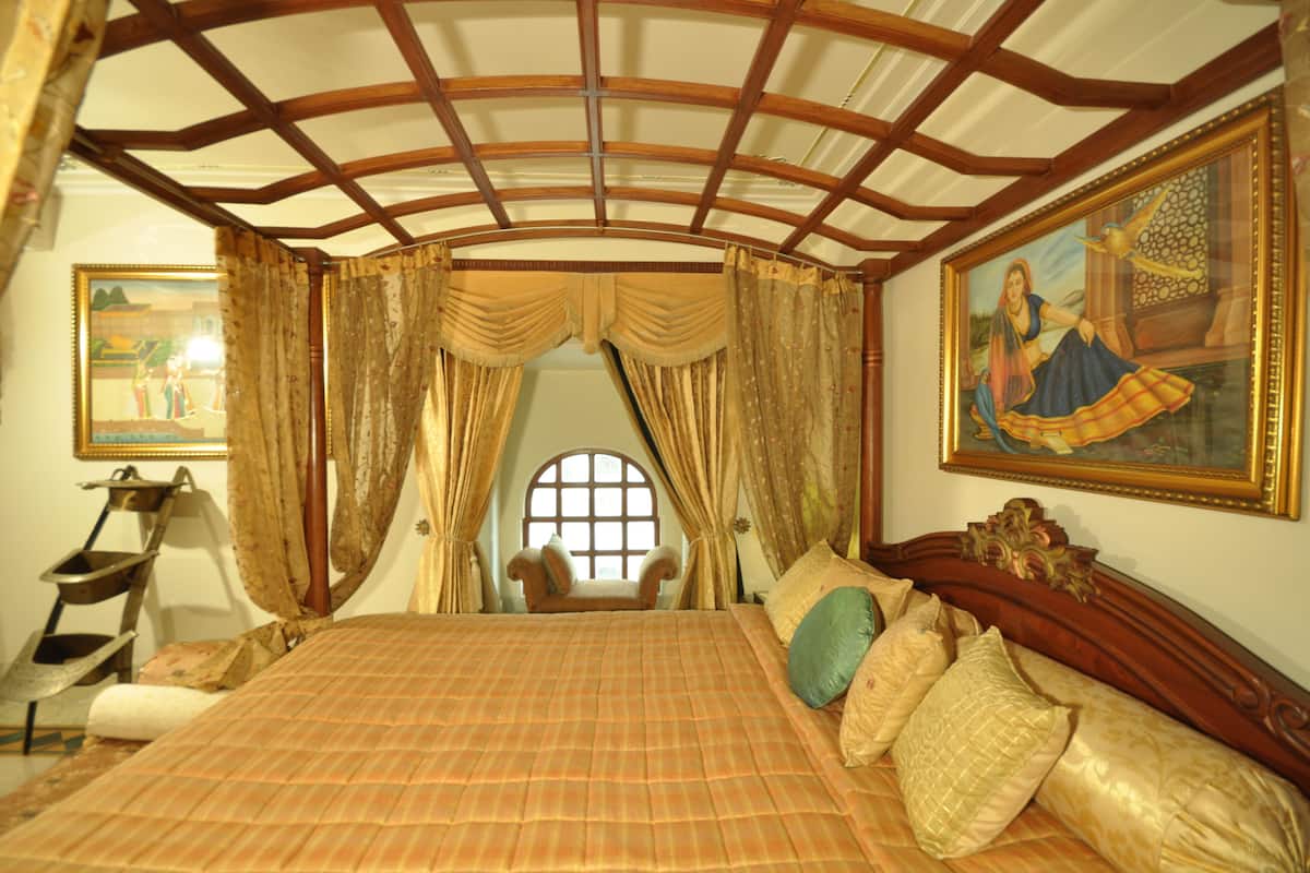 Un dormitorio con una cama grande, cortinas elaboradas, techo de madera, una ventana, una silla y un cuadro en la pared.