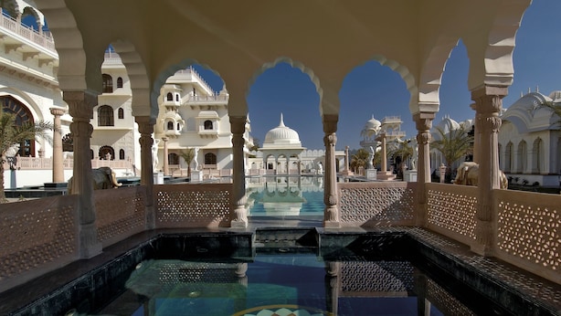 Un patio tradicional con una piscina central, arcos ornamentales y un gran edificio con cúpulas al fondo.