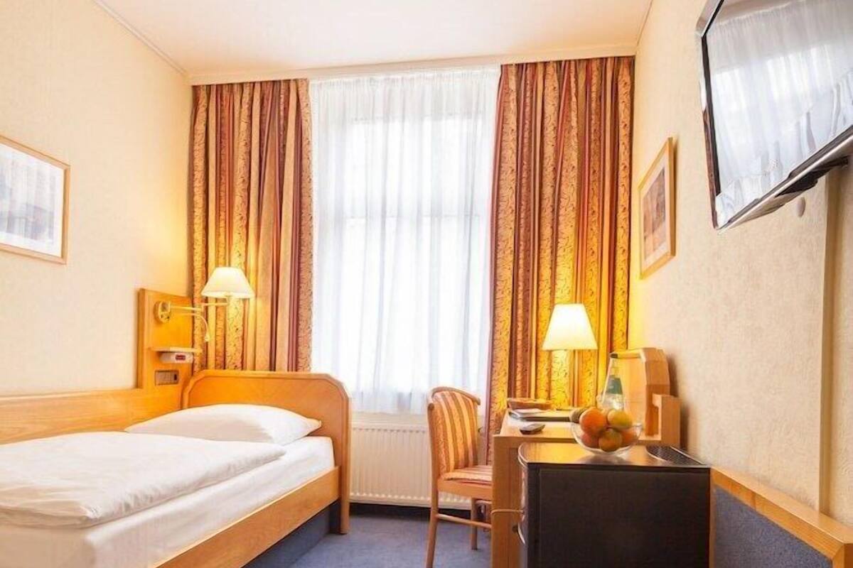 Une chambre d’hôtel comprenant un lit, un bureau avec une chaise, une télévision et un vase avec des fleurs.