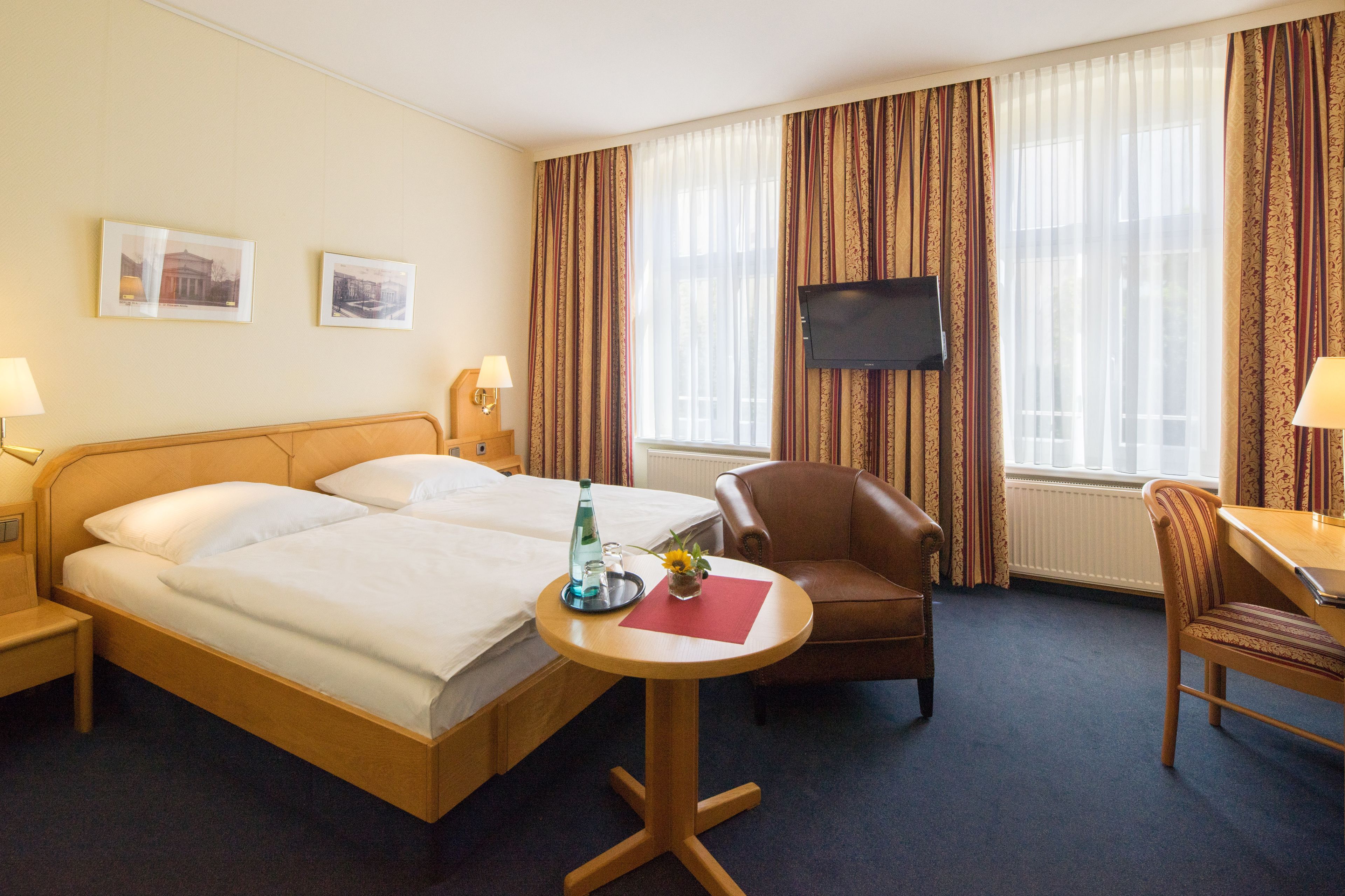 A hotel room with two beds, a TV, a desk with a chair, and a window with curtains.
