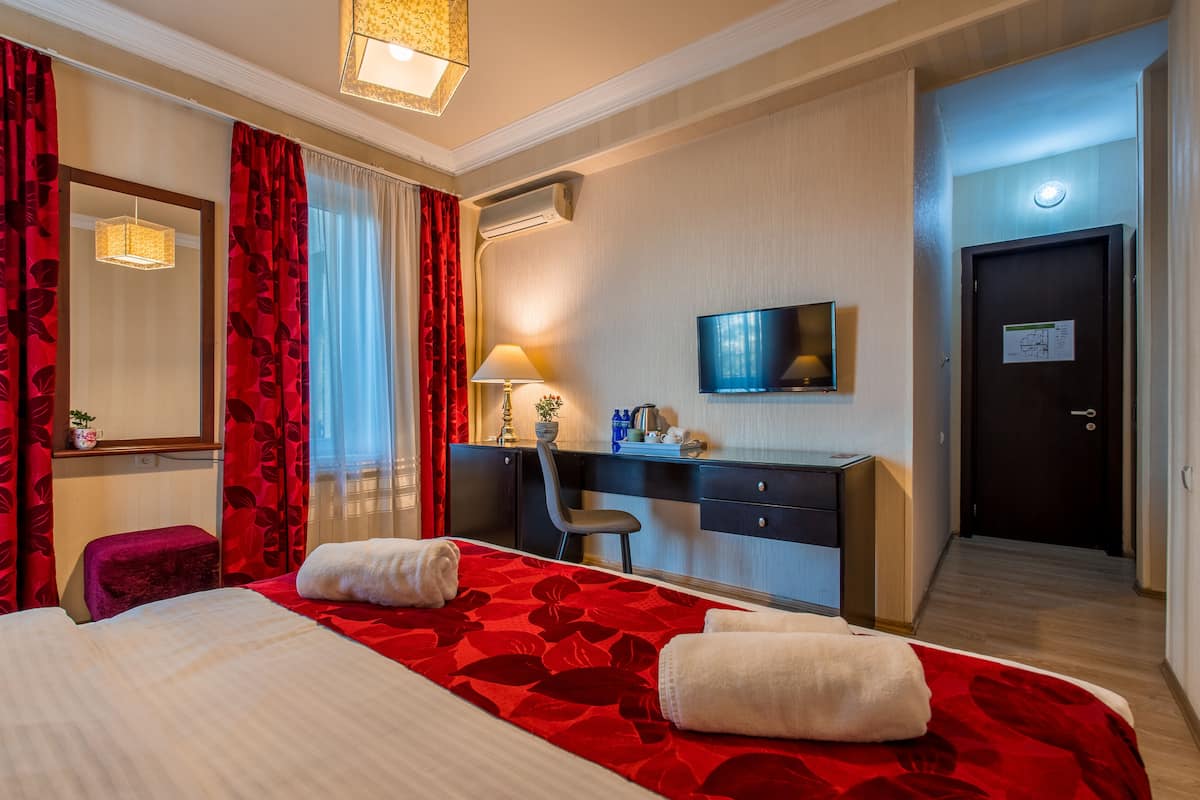 A hotel room with a large bed, a desk, a chair, a television, and a door with a key lock.