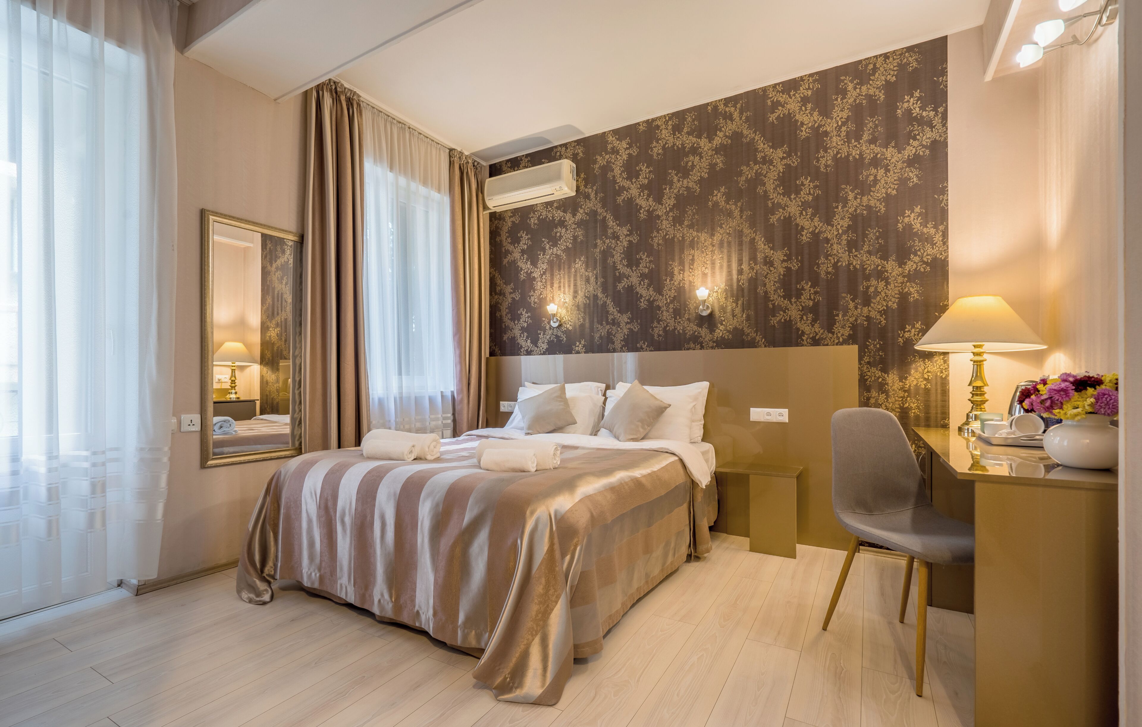 A hotel room with a large bed, a desk, a chair, and a mirror.