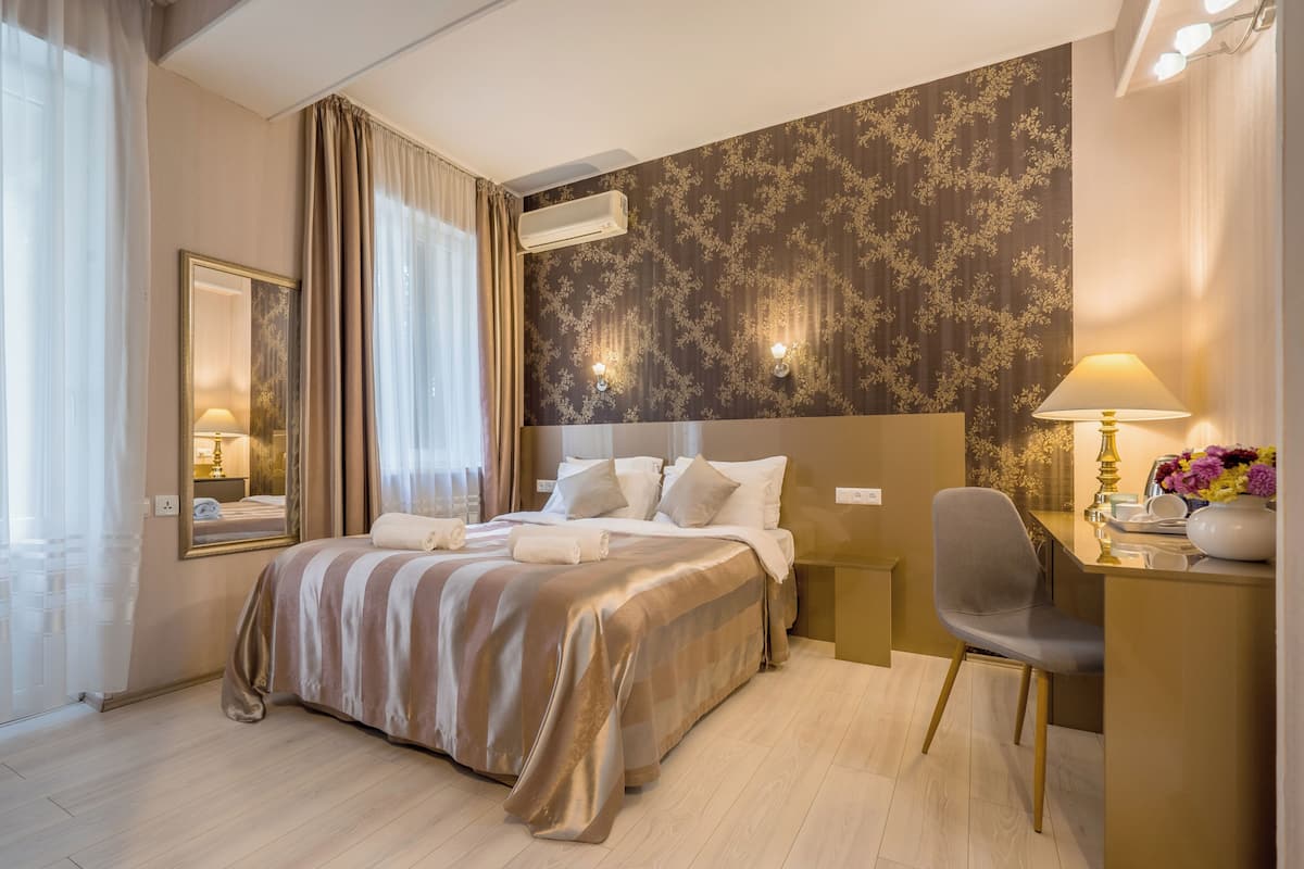 A hotel room with a large bed, a desk, a chair, and a mirror.