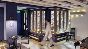 A room with a piano, a table with chairs, a bench, and a large window with decorative lights. - Iliani Hotel (Tbilisi)