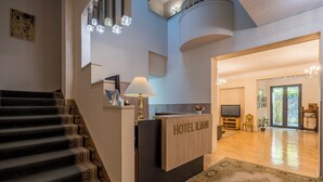 A hotel lobby with a reception desk, a staircase with patterned steps, and a large rug. - Iliani Hotel (Tbilisi)