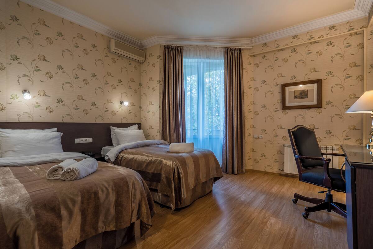 A hotel room with two beds, a desk, a chair, and a window with curtains.