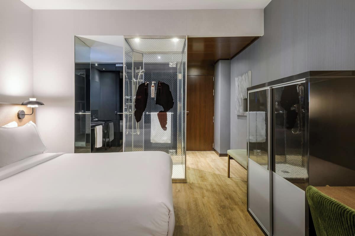 A hotel room with a bed, a wardrobe, a seating area, and a glass-enclosed shower.