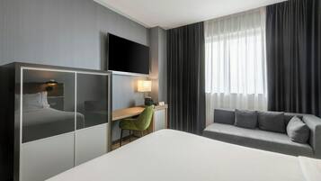 Una habitación de hotel con cama, escritorio, televisor, sofá y ventana con cortinas.