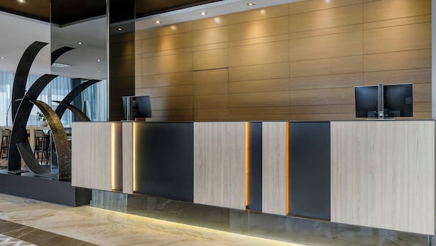A modern reception desk with a wooden panel design, integrated lighting, and a large abstract sculpture to the left.