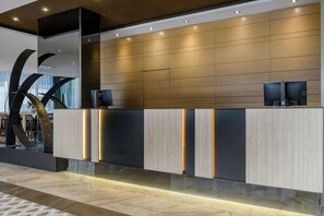 Un mostrador de recepción moderno con panel de madera, iluminación integrada y una gran escultura abstracta a la izquierda.
