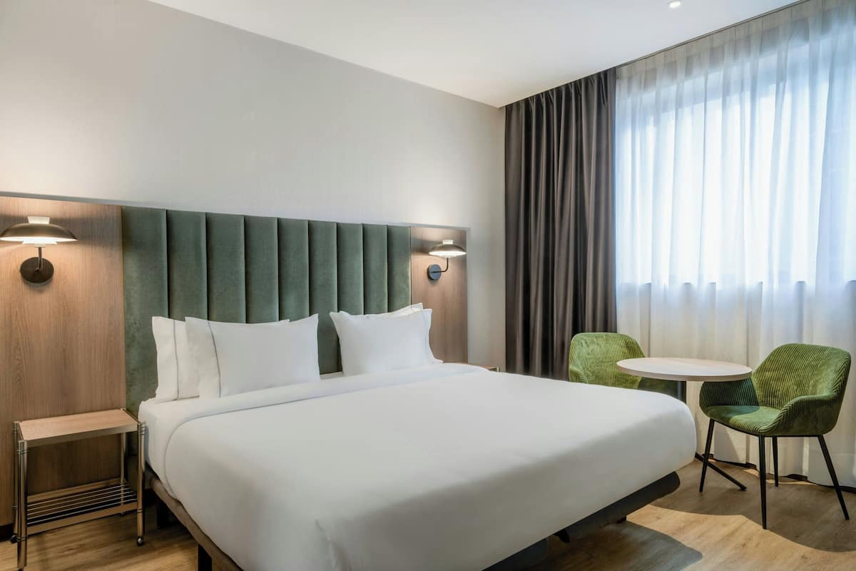 A hotel room with a large bed, two wall-mounted lamps, a small table, and two chairs.