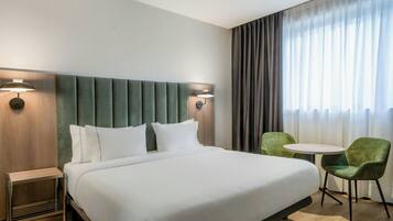 Une chambre d’hôtel avec un grand lit, deux lampes fixées au mur, une petite table et deux chaises.