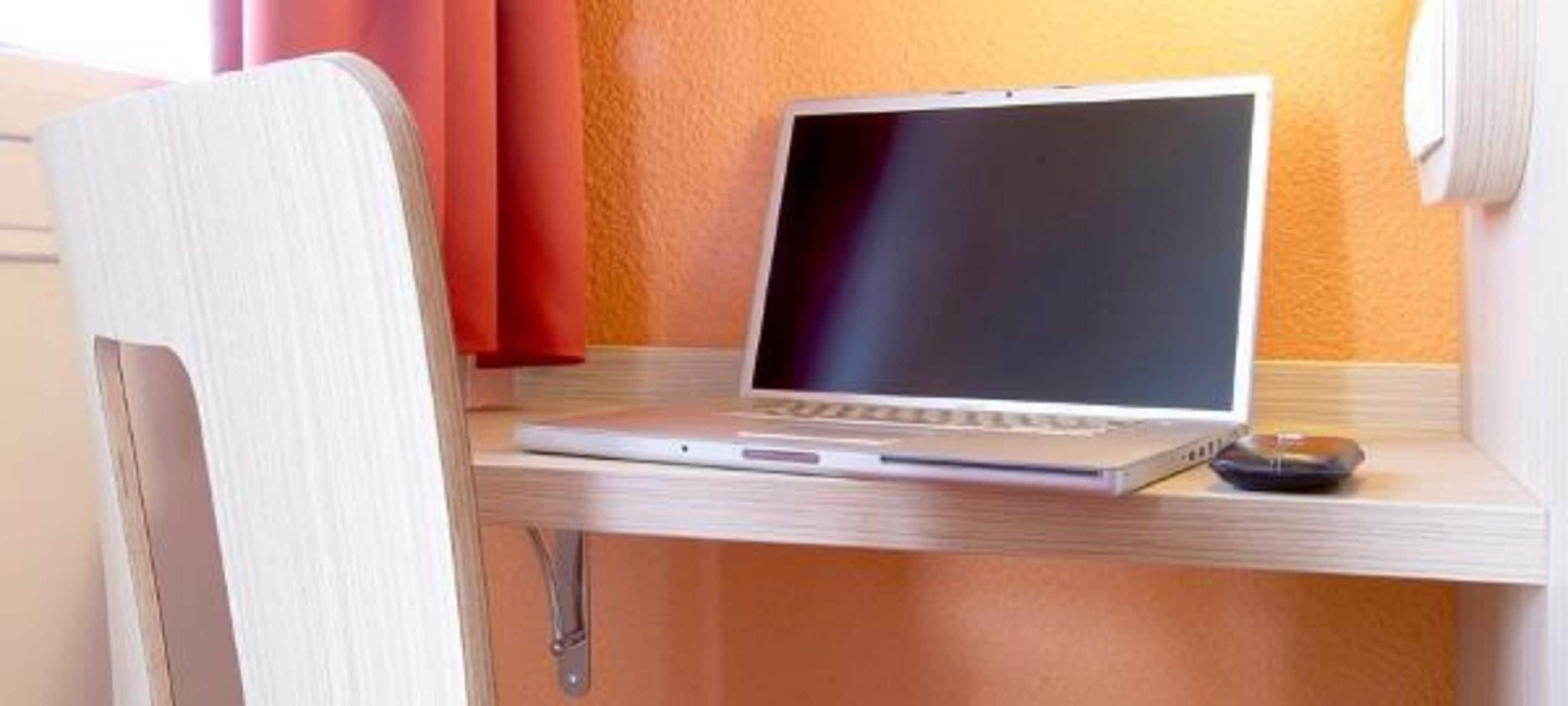 Una computadora portátil sobre un escritorio de madera con una silla.
