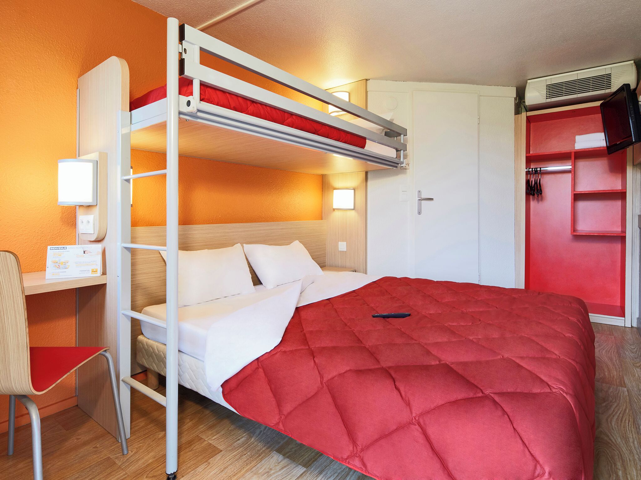Una cama litera con colchón rojo, un escritorio con silla, una mesita de noche y un armario rojo.