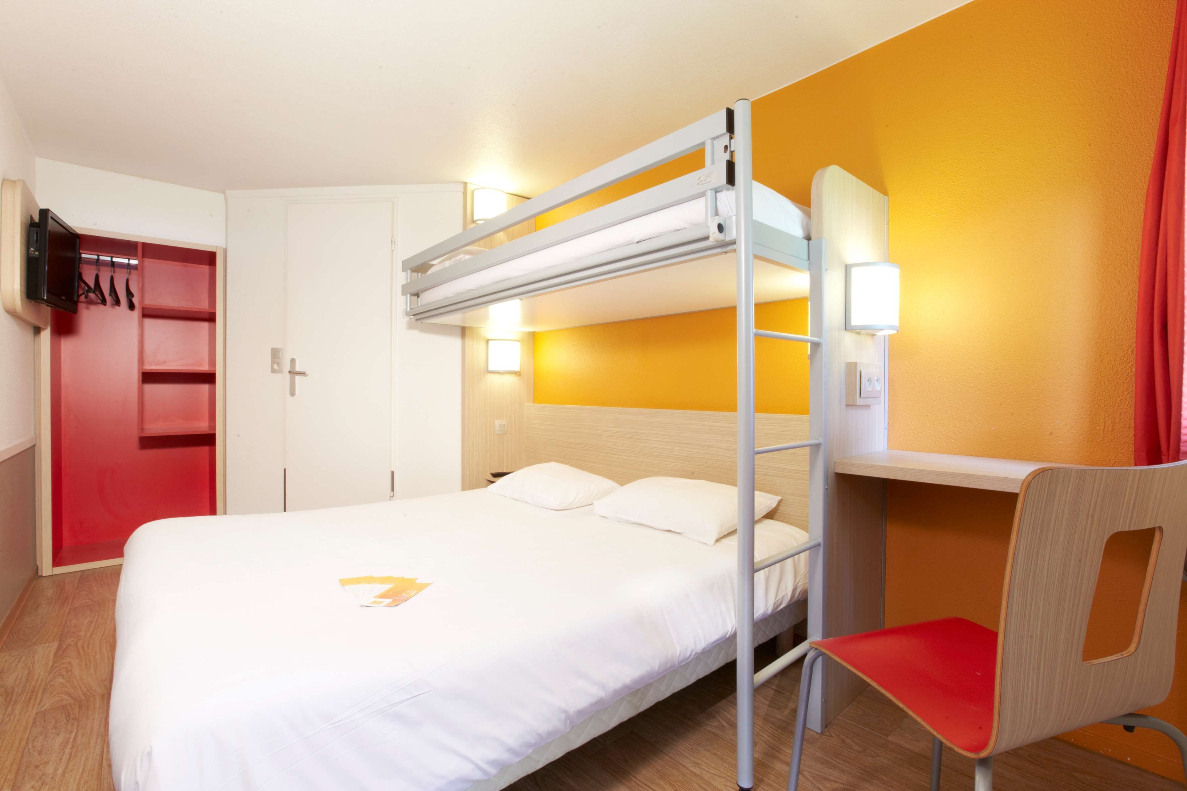 A bunk bed with a desk and chair, a television, and a red wardrobe in a hotel room.