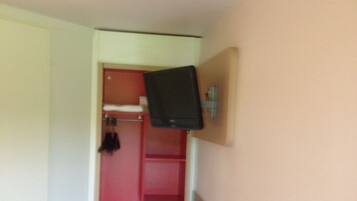 A small room with a bed, a red door, and a television mounted on the wall.