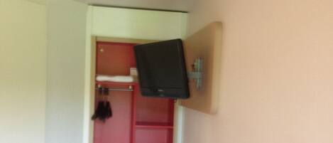 A small room with a bed, a red door, and a television mounted on the wall.