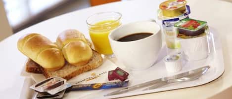 Bandeja de desayuno con panecillos, un vaso de jugo de naranja, una taza de café y una variedad de mermeladas y untables.