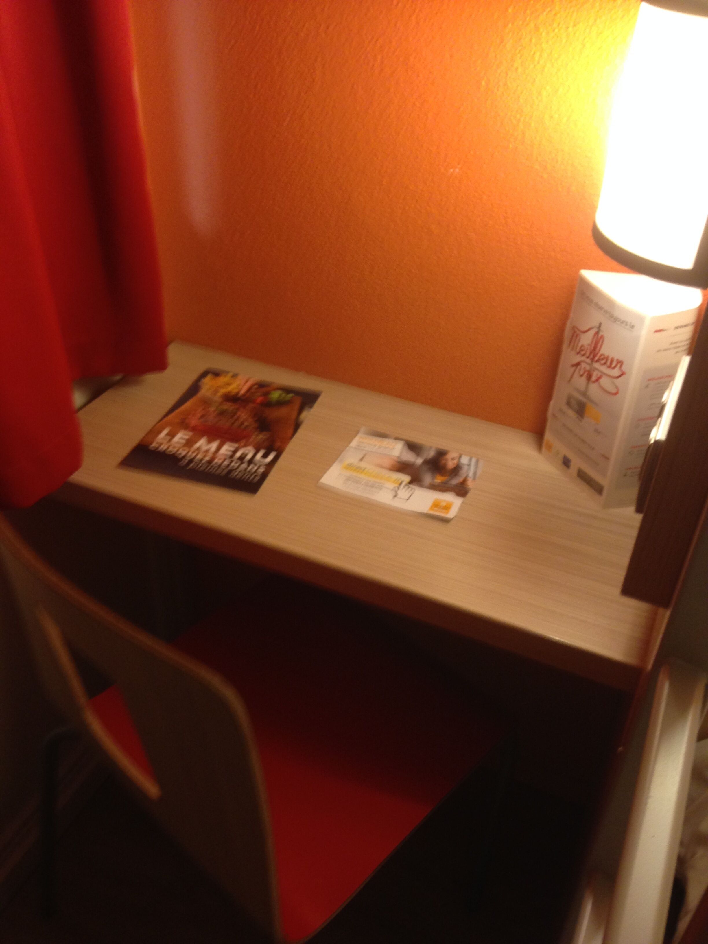 A hotel room with a wooden table, a chair, a lamp, and a magazine on the table.