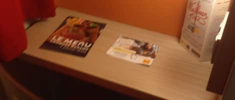 A hotel room with a wooden table, a chair, a lamp, and a magazine on the table.