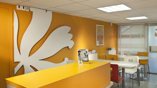 A reception area with a yellow counter, white decorative wall piece, and several tables and chairs. - Premiere Classe Charleville Mezieres (Charleville-Mezieres)