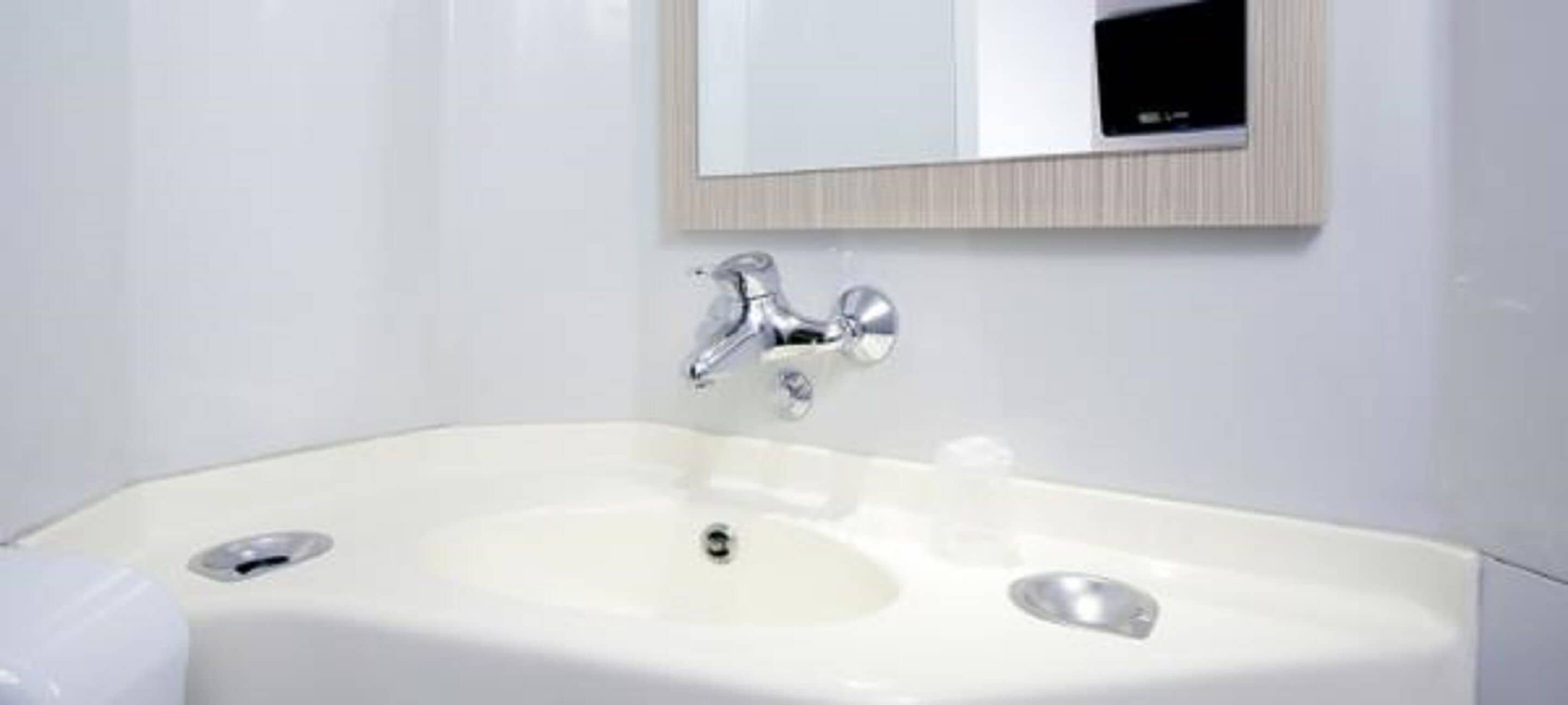 A modern bathroom with a white sink, chrome faucet, and a mirror above it.
