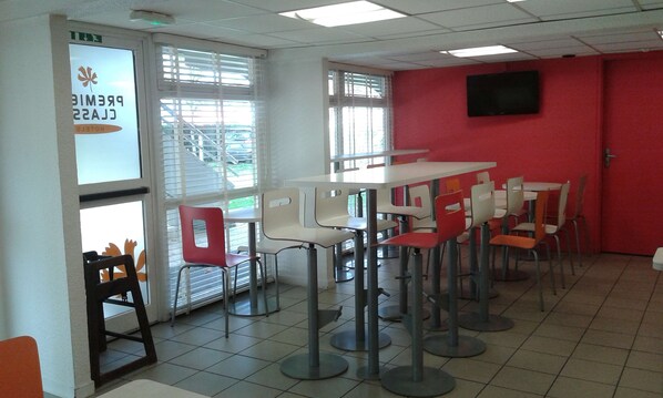 A dining area with tables and chairs, a red wall, and a sign indicating a restaurant.