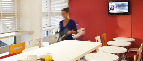 A breakfast area with a long table, chairs, and a TV screen.