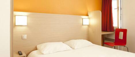 Habitación de hotel con cama, mesita de noche, una silla roja y una ventana con cortinas.