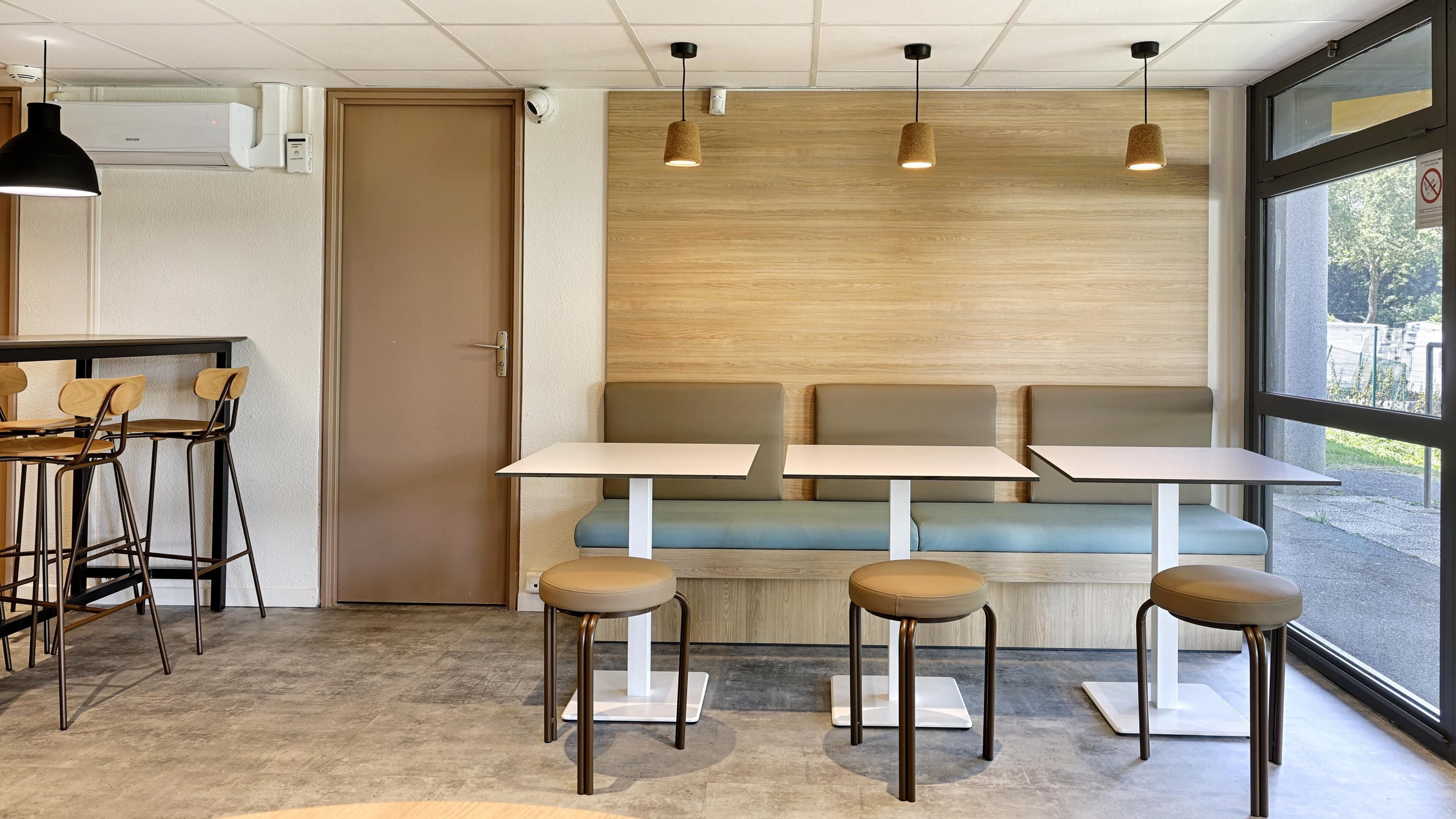 Een modern café interieur met een houten wand, een zithoek met tafels en stoelen, en een groot raam.