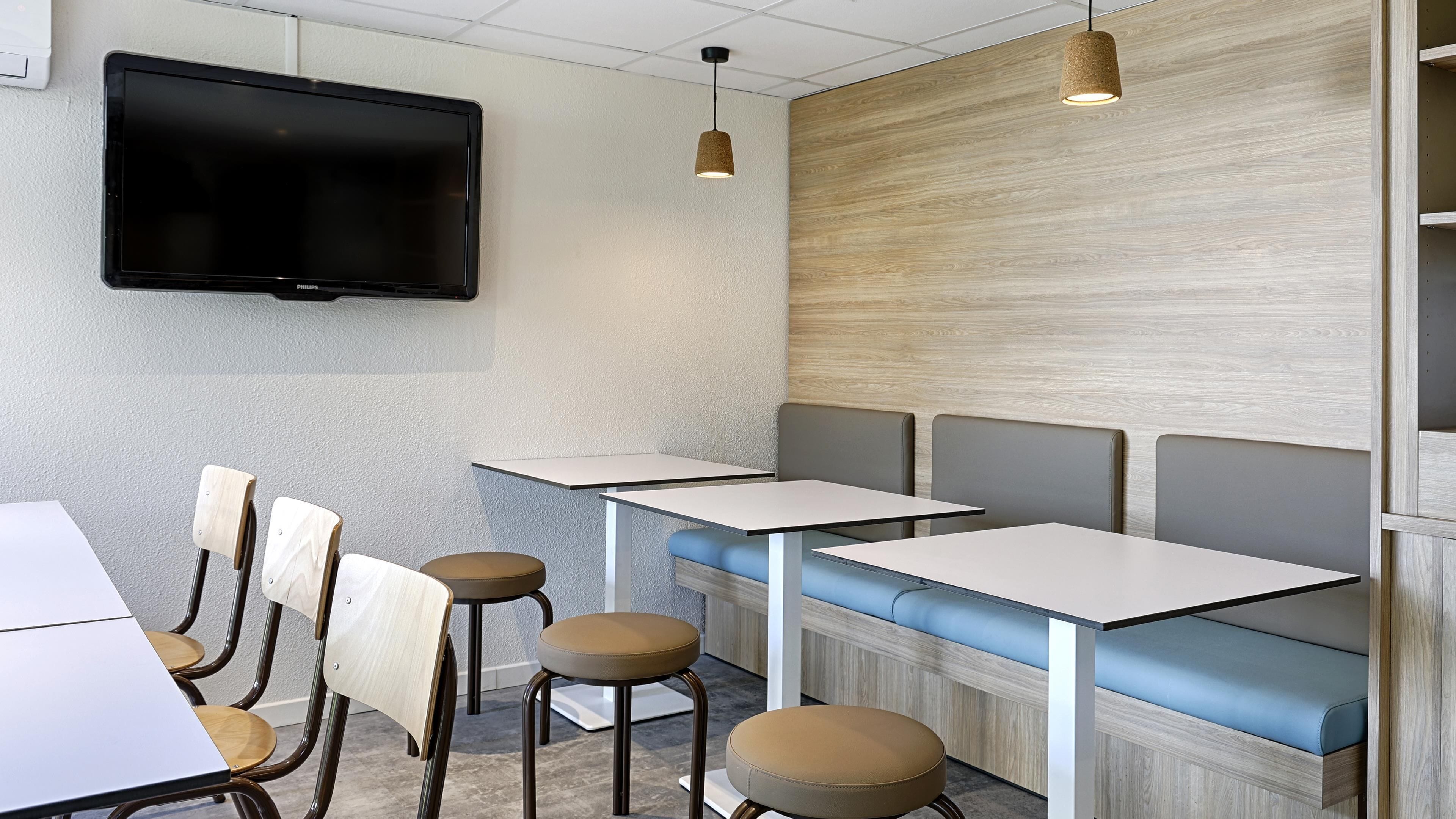 Un interior de restaurante con una televisión de pantalla plana, mesas, sillas y una zona de estar con bancos acolchados.