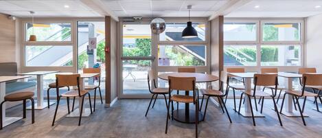 A modern dining area with tables and chairs, large windows, and a view of the outdoors.
