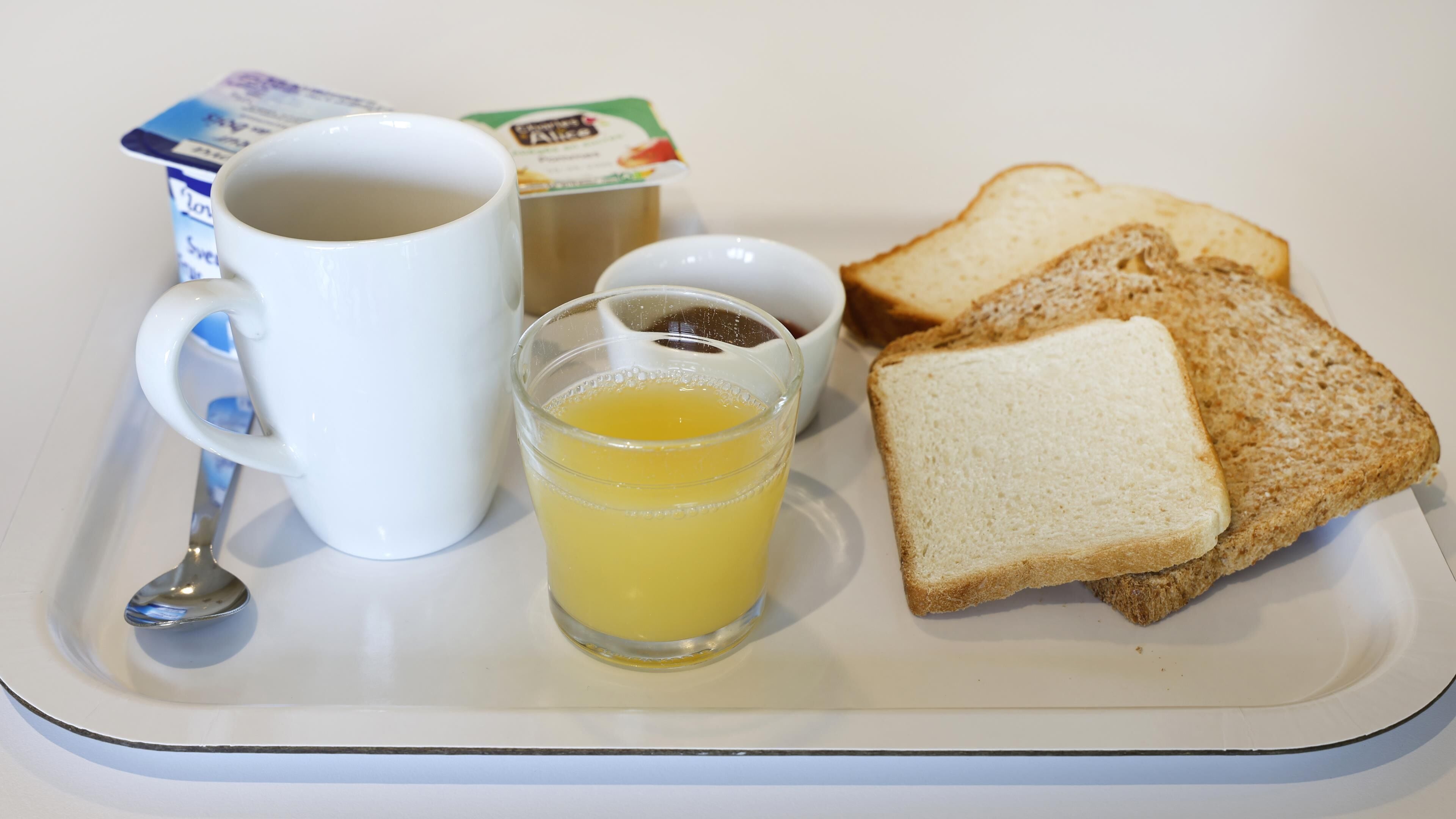 A tray with a white mug, a glass of orange juice, two slices of white bread, and a small container of butter.