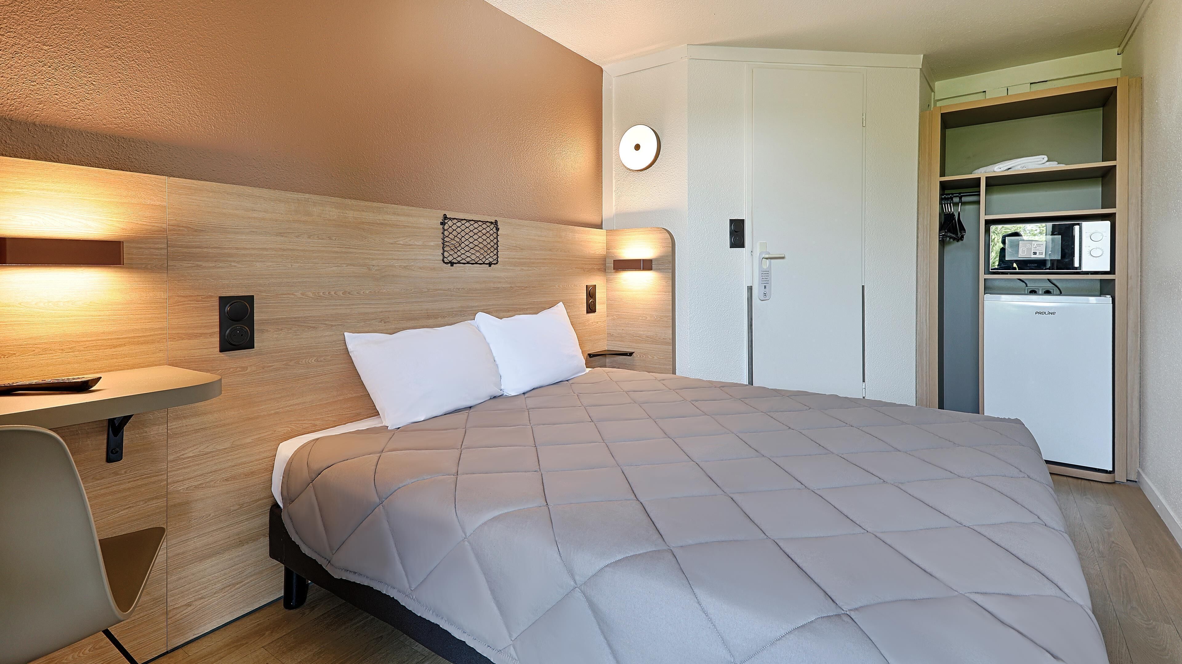 Een hotelkamer met een bed, nachtkastje, wandlamp en een ingebouwde minibar.