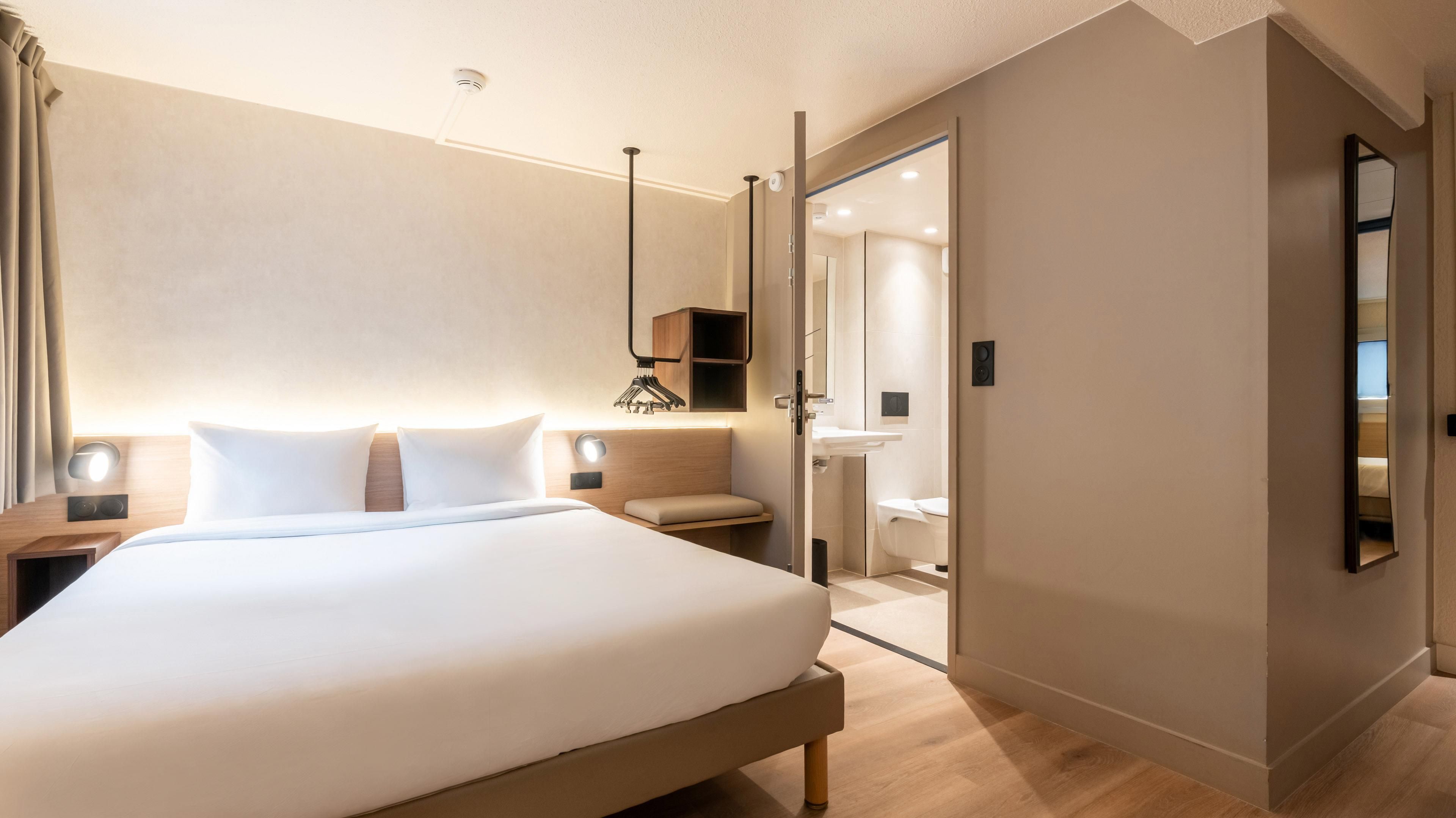 A hotel room with a large bed, bedside tables, a nightstand, a wardrobe, a mirror, and a bathroom with a sink and toilet.