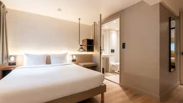 Een hotelkamer met een groot bed, nachtkastjes, een kledingkast, een spiegel en een badkamer met wastafel en toilet.