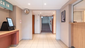 A hotel reception area with a digital kiosk, a 'CK IN' sign, a no-smoking sign, and a staircase leading to another floor. - Kyriad ECO - Montreuil (Montreuil)