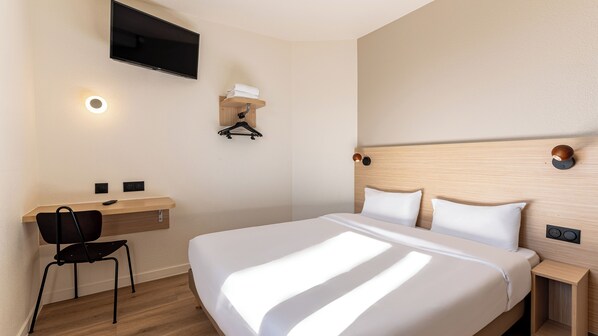 Habitación de hotel con cama, un escritorio con silla, televisor montado en la pared y una lámpara de pared.