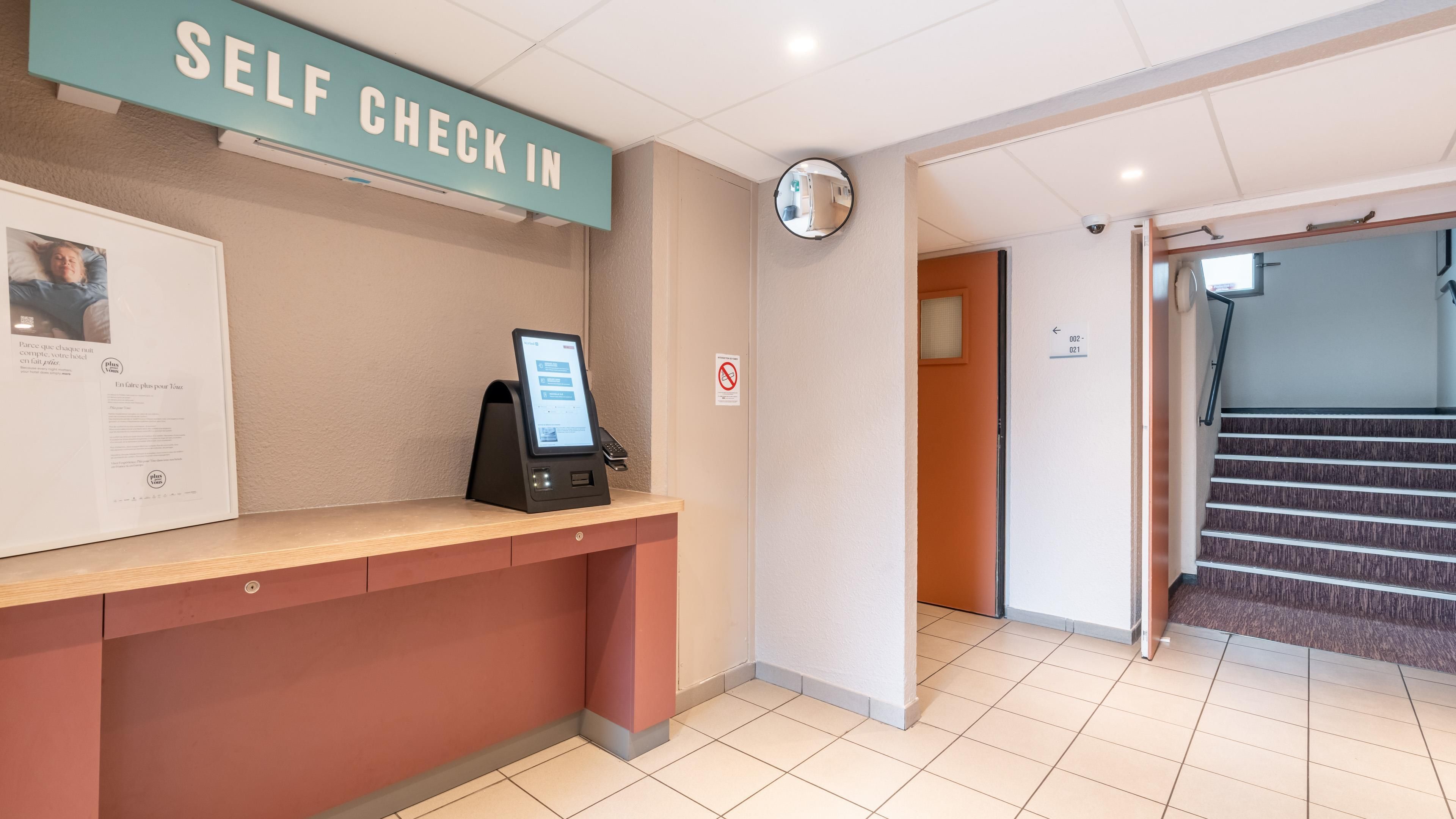 Een zelf incheck balie met een digitale kiosk, een ingelijste informatieposter en een rookverbods bord.