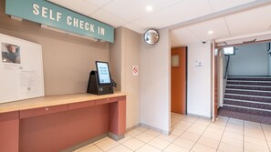 A self-check-in counter with a digital kiosk, a framed informational poster, and a no-smoking sign. - Kyriad ECO - Montreuil (Montreuil)