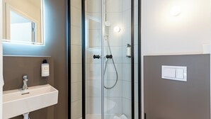 A bathroom with a glass-enclosed shower, a sink with a soap dispenser, and a light switch on the wall. - Kyriad ECO - Montreuil (Montreuil)